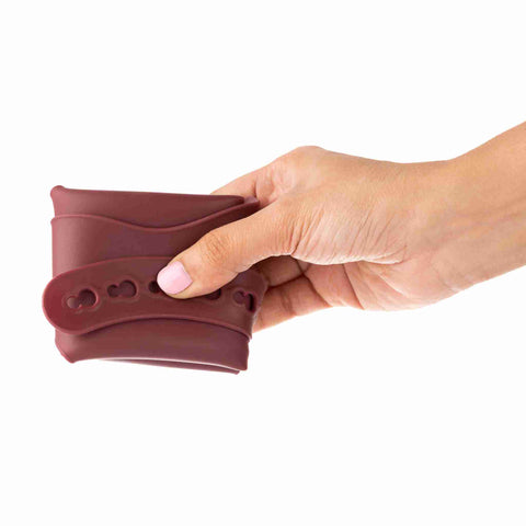 Burgundy soft silicone bib by eco rascals folded up and held in someone's hand 