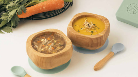 Picture shows two bowls of chicken and vegetable soup in bamboo eco rascals suction bowls. One soup has been blended and one soup is a clear broth with vegetables. 