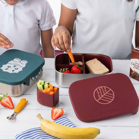 Image shows the Classic Burgundy Lunchbox by eco rascals with removable dividers and a stainless steel base with a child taking a carrot from the box. 