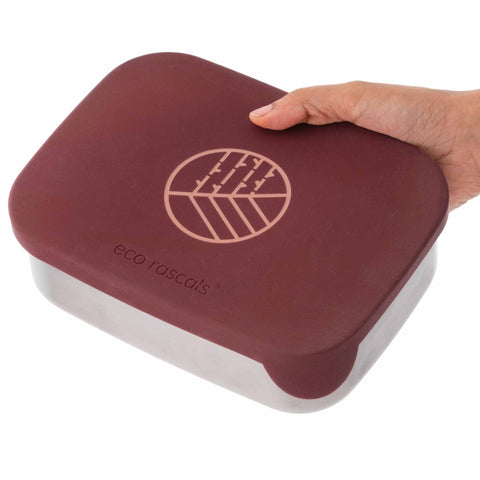 Image shows the Classic Burgundy Lunchbox by eco rascals with removable dividers and a stainless steel base being held closed by an adult hand.