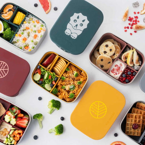 Image shows a variety of different lunchboxes filled with food such as pancakes, strawberries, pomegranate, figs, pasta, crackers, salad, apple, rice, corn etc.