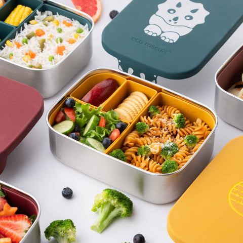 Image shows the classic Mustard eco rascals lunch box bento style with removable dividers with food inside, alongside the dinosaur teal lid and the burgundy lid to depict a range.