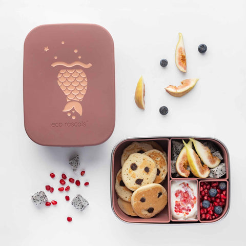 Image shows the mermaid lunchbox by eco rascals with pancakes, figs, dragon fruit, pomegranate, blueberries and yoghurt spread across the four removable silicon lunchbox organisers. The Lids is rest to the left side of the lunchbox. 