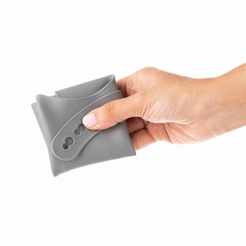 Grey/Silver soft silicone bib for kids folded up and held in a person's hand. 